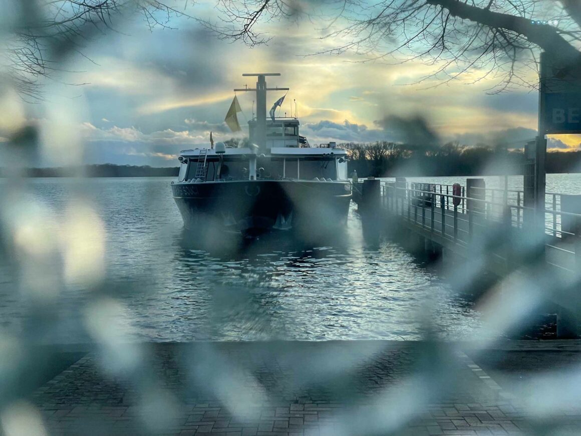 magical view through broken glass towards lake bathed in sunset and a ferry docking at quay 